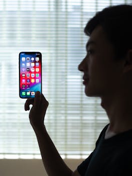 Profile of a man holding a smartphone with colorful apps, backlit indoors.